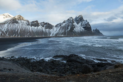 Scenic view of sea by mountain against sky