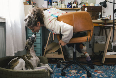 Woman kissing dog while sitting on chair at home