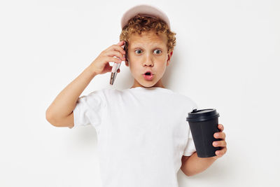 Boy holding coffee cup talking on phone standing against white background