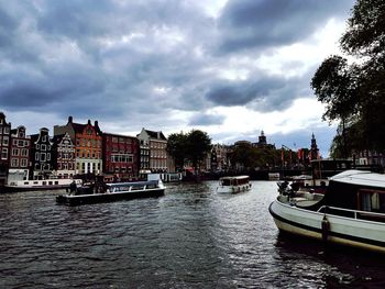 Boats in river by buildings in city against sky