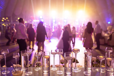 Foreground focus vases on glass table with dancing people at wedding