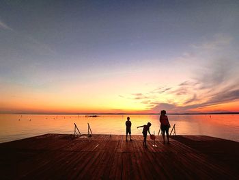 Silhouette people walking at beach against sky during sunset