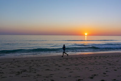 Silhouette person on beach against sky during sunset