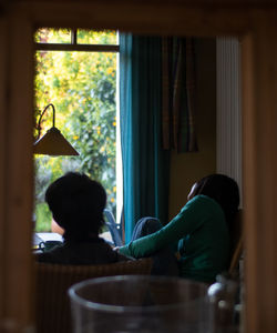 Rear view of people in glass window at home