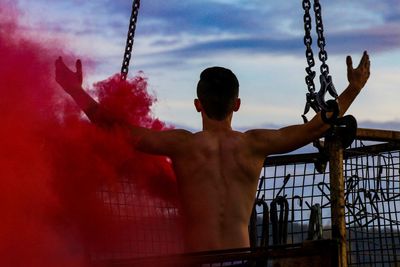 Rear view of shirtless man with arms outstretched with distress flare on metal