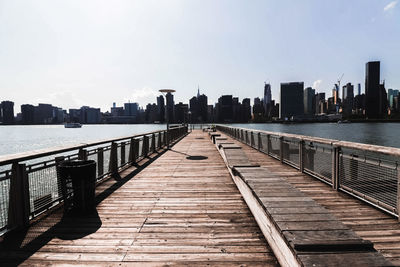 Pier over river amidst buildings in city against sky