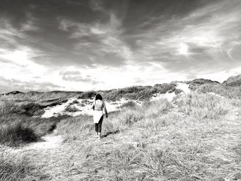 Rear view of woman walking on field against sky