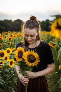 Portrait of woman standing by sunflower on field