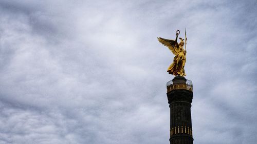 Low angle view of statue of tower against cloudy sky