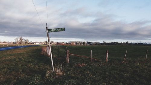 Road sign on field against sky