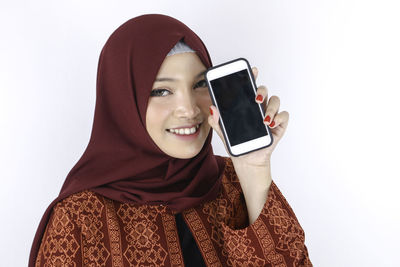 Portrait of smiling young woman using smart phone against white background