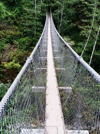 Footbridge in forest against sky