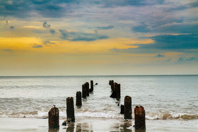 Wooden posts on sea against sky during sunset