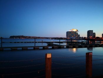 Illuminated bridge over river by buildings against sky at dusk