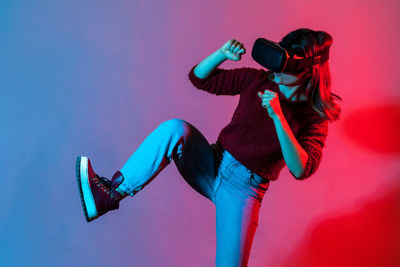 Woman wearing virtual reality simulator while standing against colored background