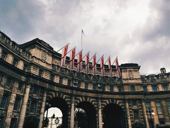 Low angle view of british flags on admiralty arch against cloudy sky