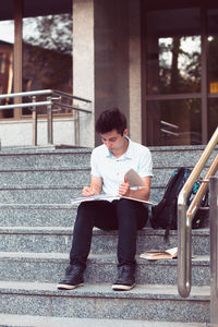 Full length of young university student studying while sitting on staircase