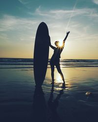 Man standing at beach against sky during sunset