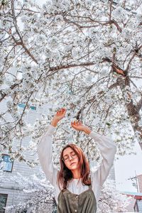 Young woman with arms raised standing against cherry blossom tree