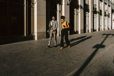 Male and female coworkers discussing while walking on footpath during sunny day