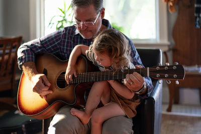 Grandfather playing guitar with granddaughter at home