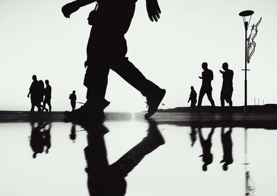 Silhouette people walking on beach against clear sky