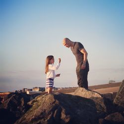 Father with daughter standing on rocks against clear sky