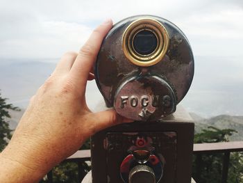 Close-up of hand holding binoculars against sky