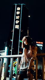 Woman standing by illuminated city at night