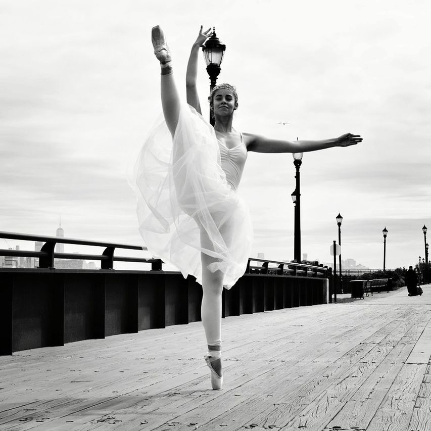 FULL LENGTH OF YOUNG WOMAN DANCING AGAINST WHITE SKY