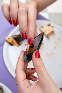 Woman with red nail polish holding mussel over plate at table