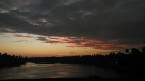 Silhouette landscape against calm sea at sunset