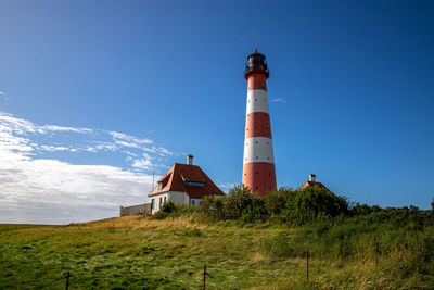 Low angle view of lighthouse on field by building against sky