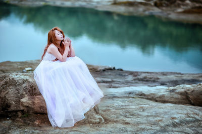 Portrait of smiling young woman standing on rock by water