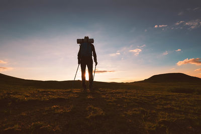 Silhouette man photographing on field against sky during sunset