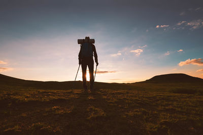 Low angle view of silhouette hiker standing on landscape against sky during sunset
