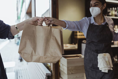 Female owner giving take away food to customer at deli shop