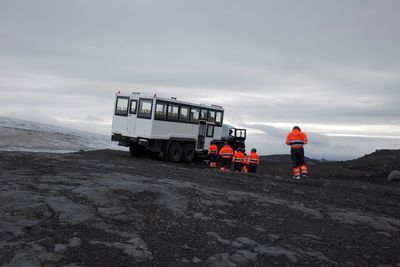 Rear view of workers walking towards vehicle against cloudy sky