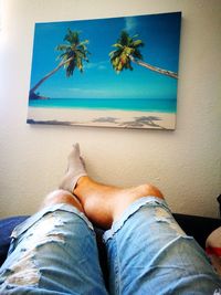 Low section of man relaxing on palm tree by sea