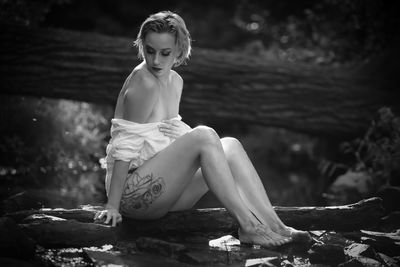 Seductive woman sitting on log in forest