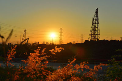 Silhouette plants by electricity pylon against sky during sunset