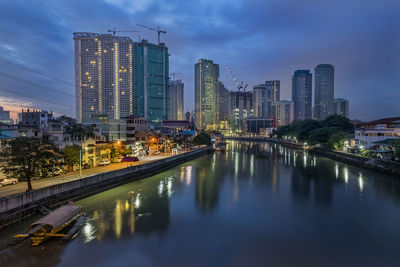Illuminated buildings by river against sky in city