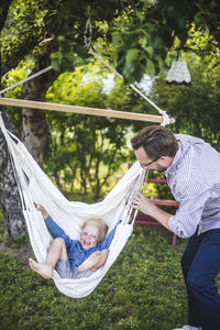 Mature father swinging son in backyard during weekend