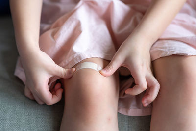 Close up of children putting court plaster adhesive bandage on her knee at home