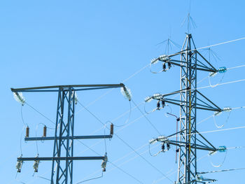 Low angle view of electricity pylon against clear blue sky