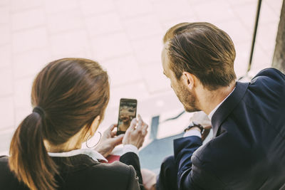 Rear view of business people looking in phone while sitting outdoors