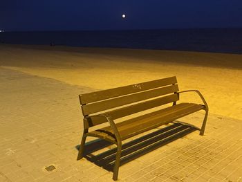 Empty bench on beach against sky at night