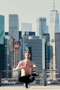 Full length of shirtless mature man practicing yoga on building terrace against one world trade center