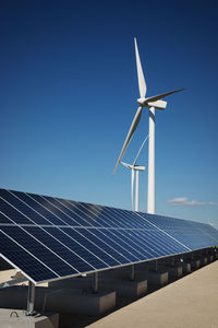 Solar panels on factory by windmills against blue sky