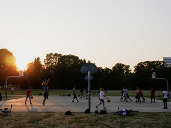 People playing soccer against sky during sunset